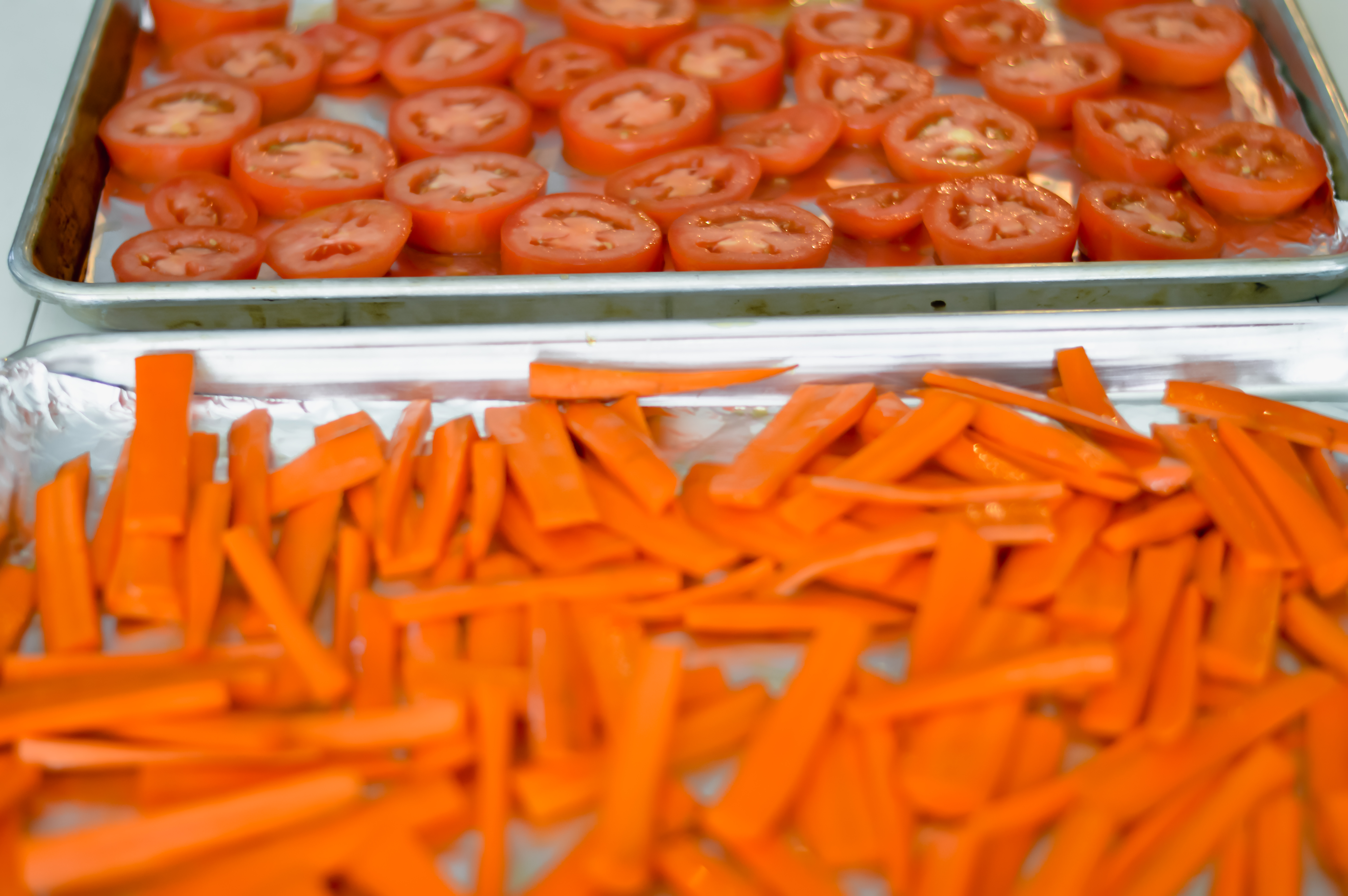carrots and tomatoes on sheet pans waiting to be roasted