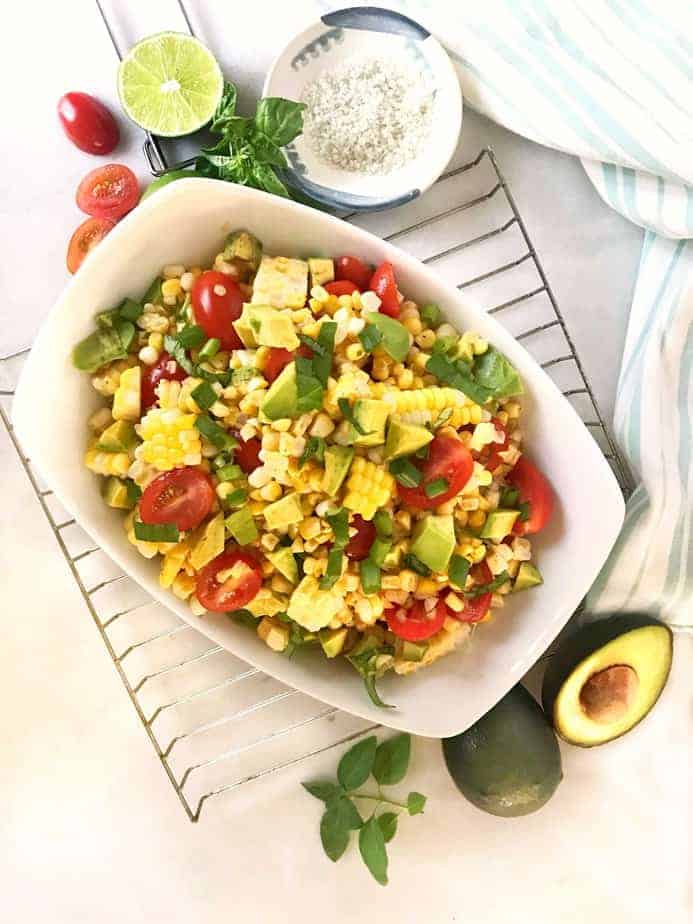 rack with white bowl of corn, tomato, avocado salad and fixings.