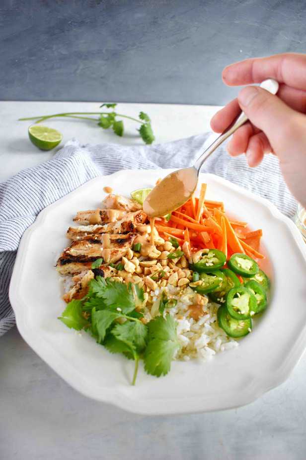 thai rice bowl with peanut sauce being drizzled over top