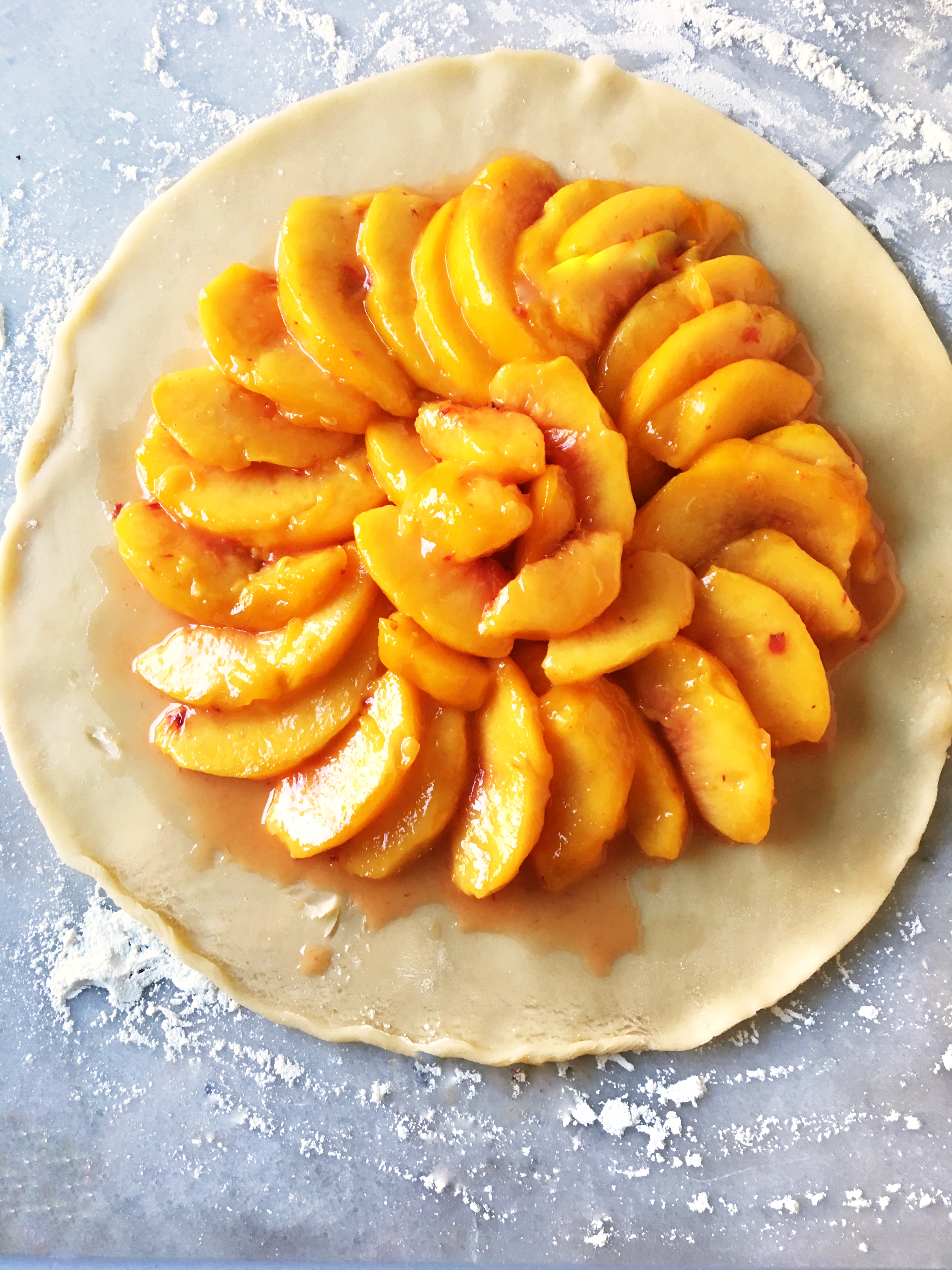 fresh peaches laid in a spiral over round pastry crust