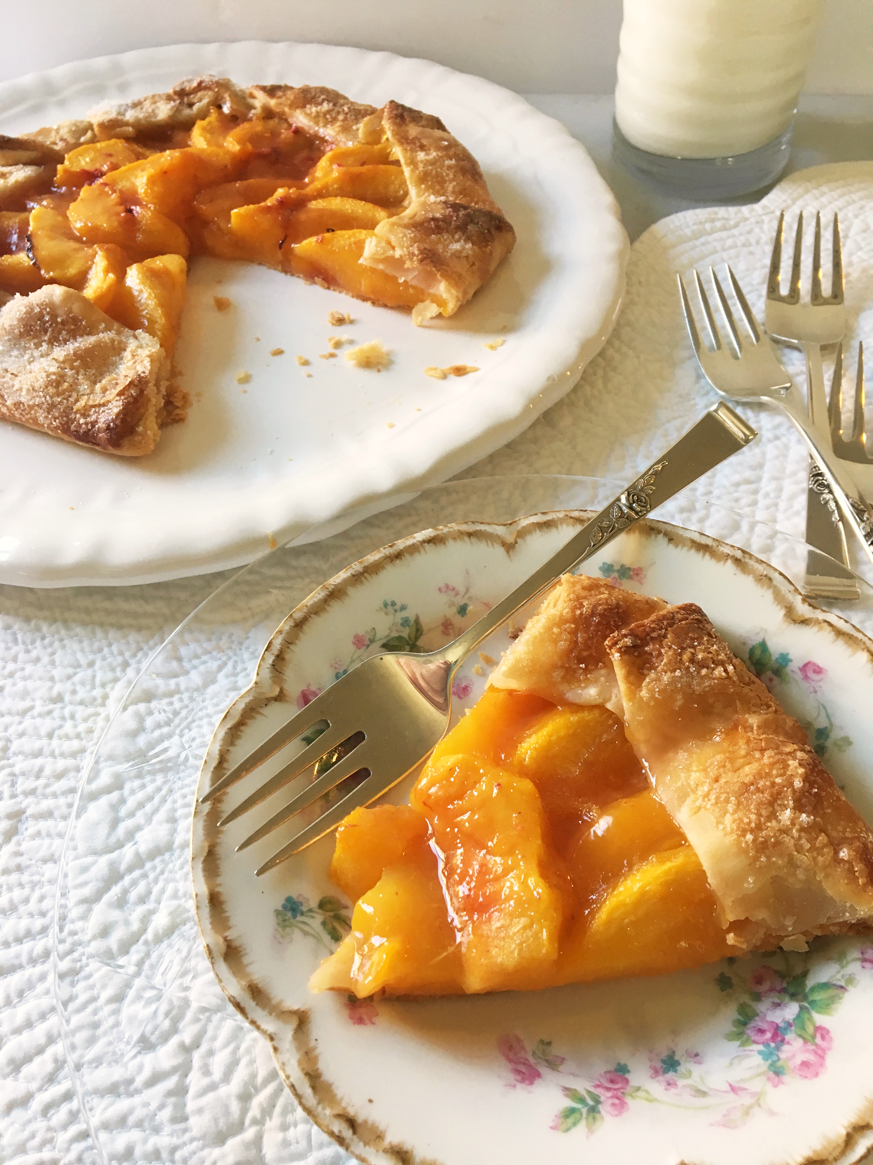 Slice of fresh peach galette on small plate with platter and remaining galette.