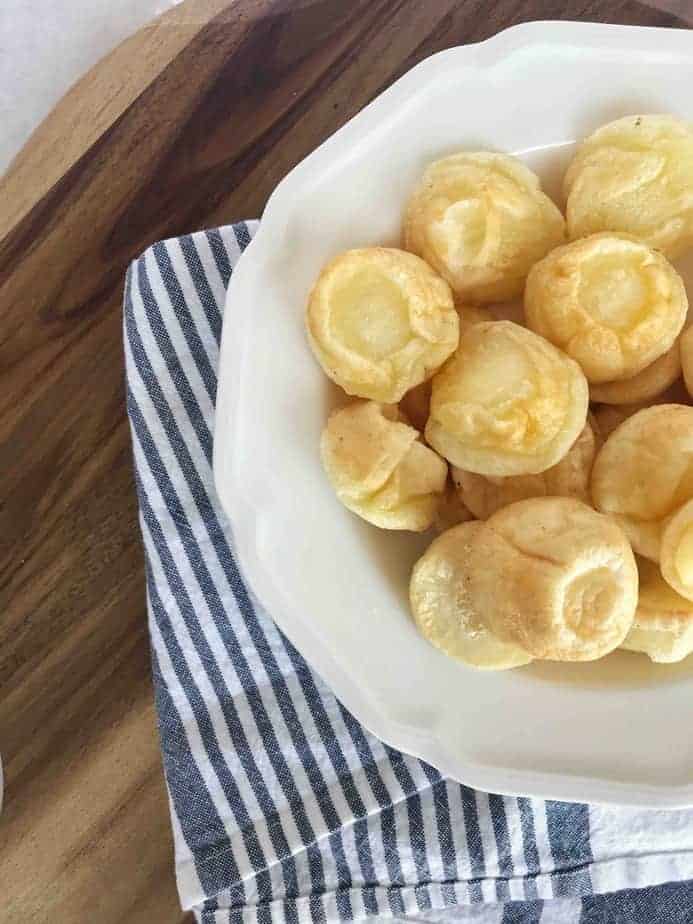 cheese breads sitting in a white bowl on a wooden board