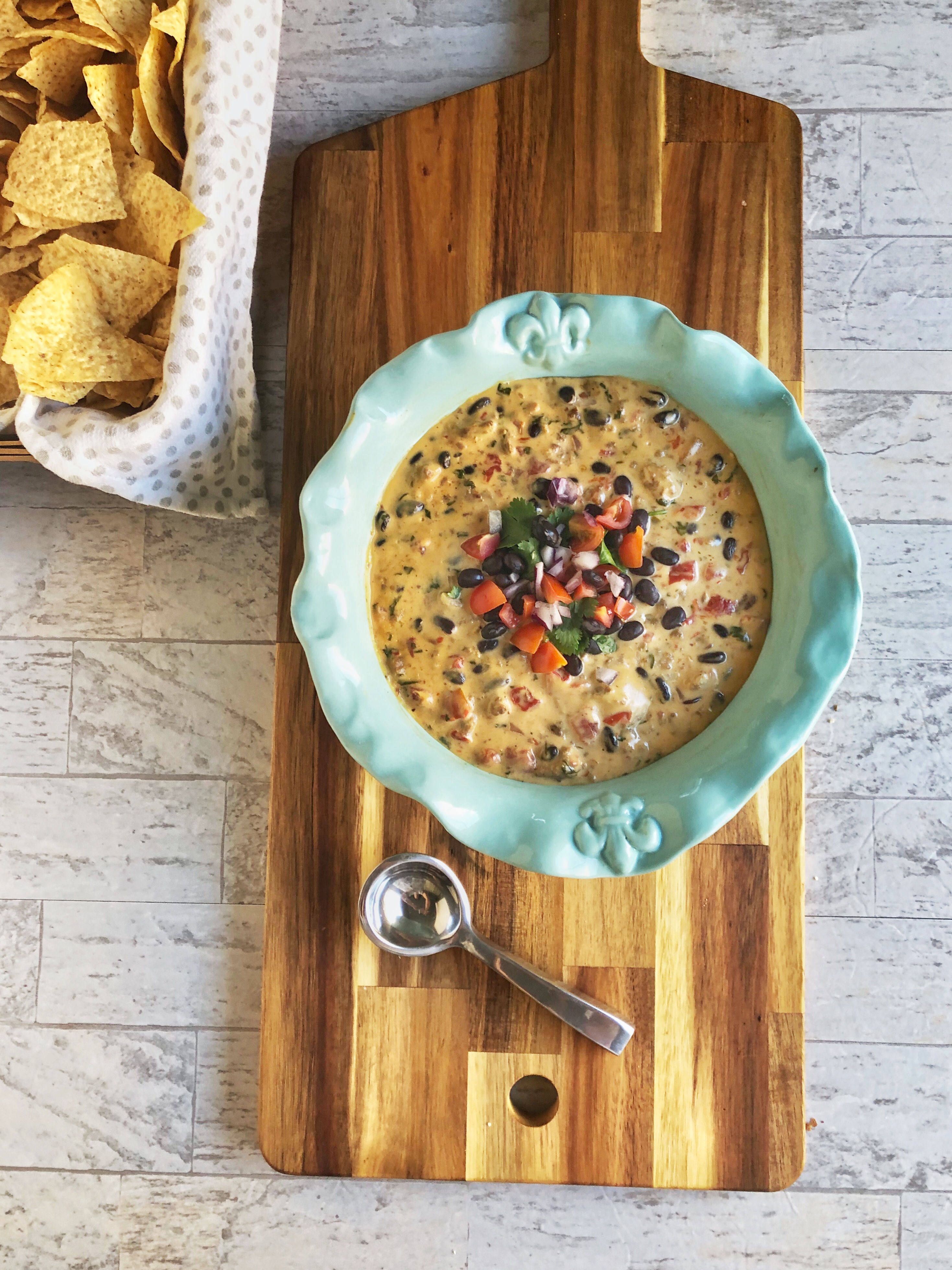 bowl f ultimate queso dip on a cutting board with basket of tortilla chips