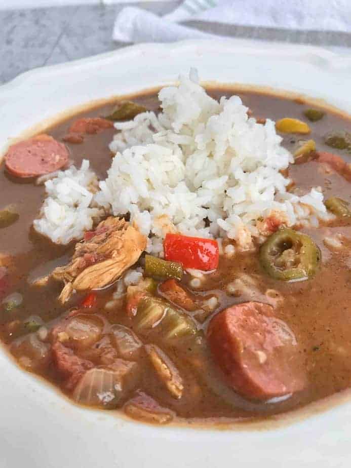 chicken and sausage creole gumbo in white bowl with rice on top