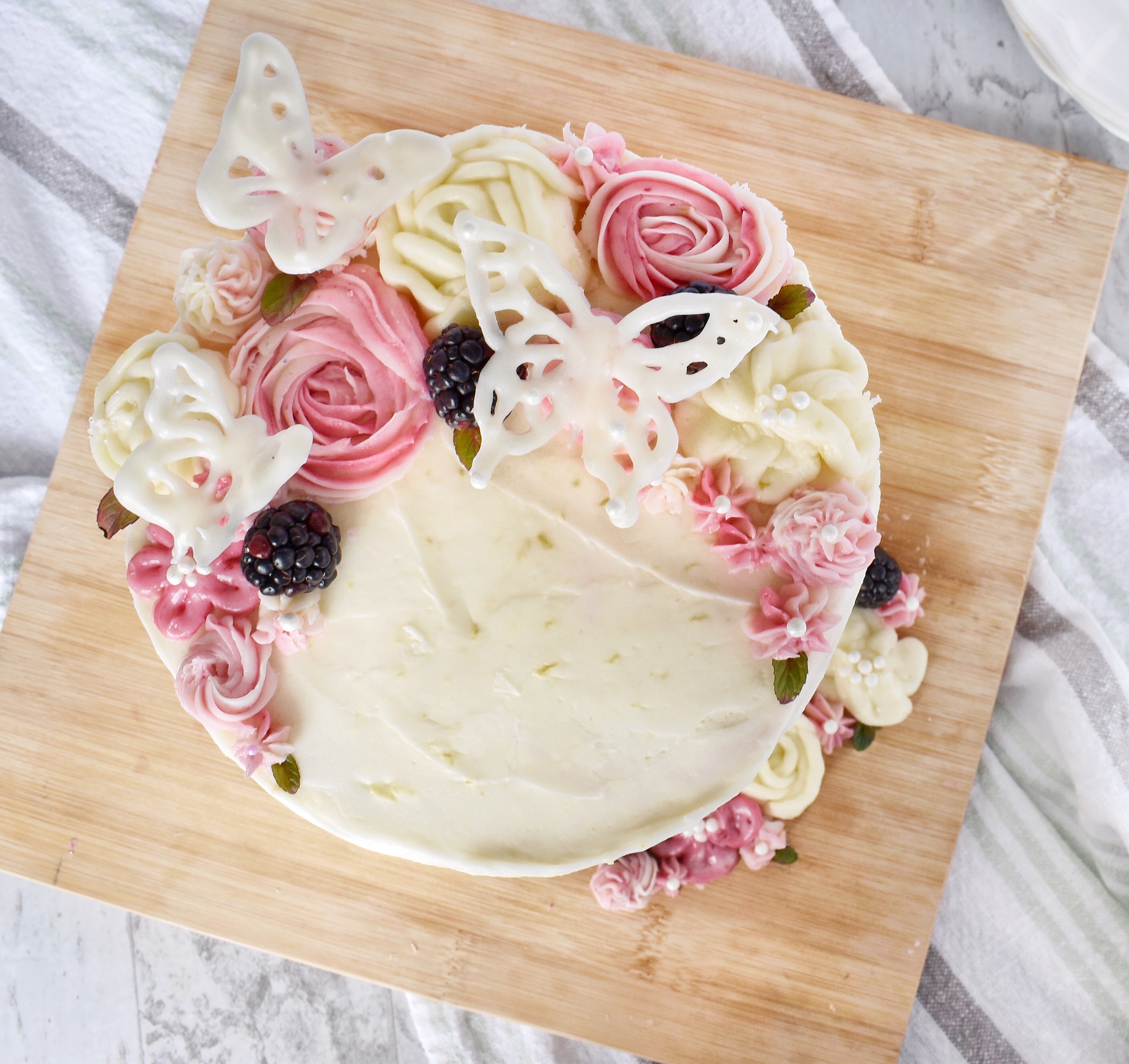 blackberry lemon poppyseed cake topped with frosting flowers and white chocolate butterflies