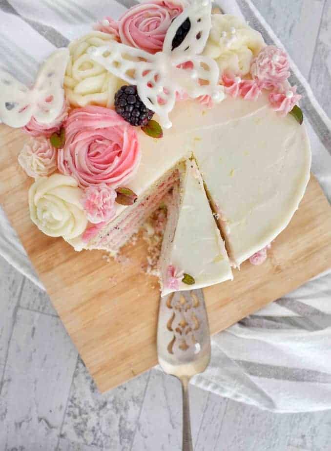overhead shot of blackberry lemon poppyseed cake with pink and white buttercream flowers and white chocolate butterflies