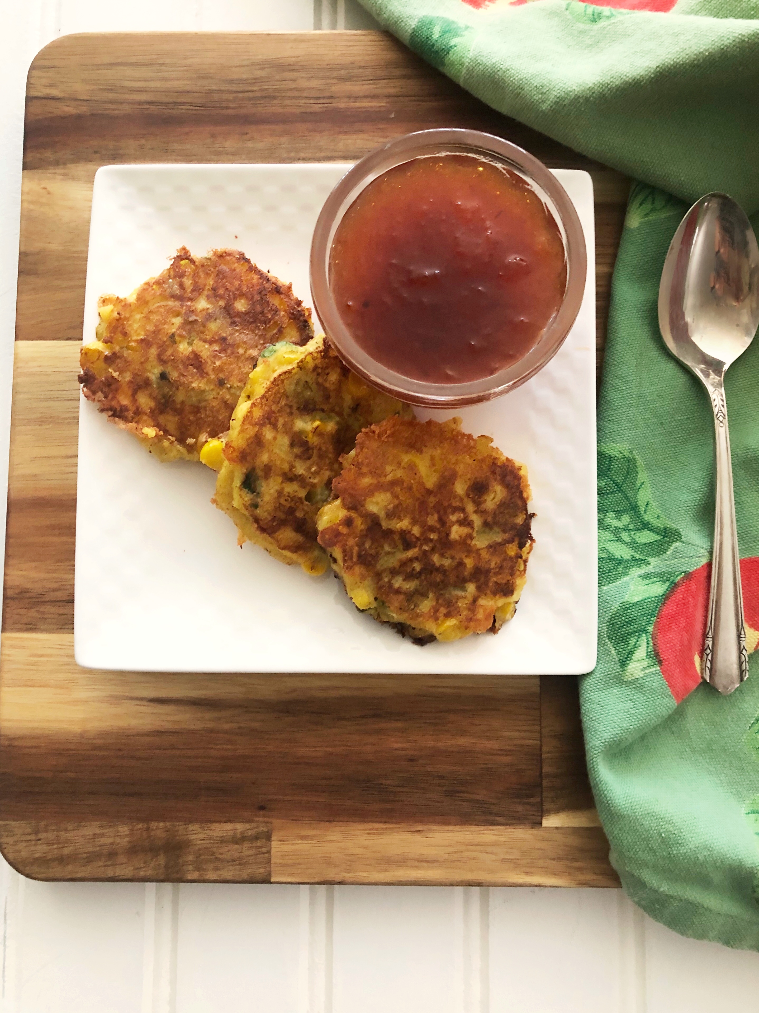 corn fritters on a plate with green napkin, spoon and peach sauce