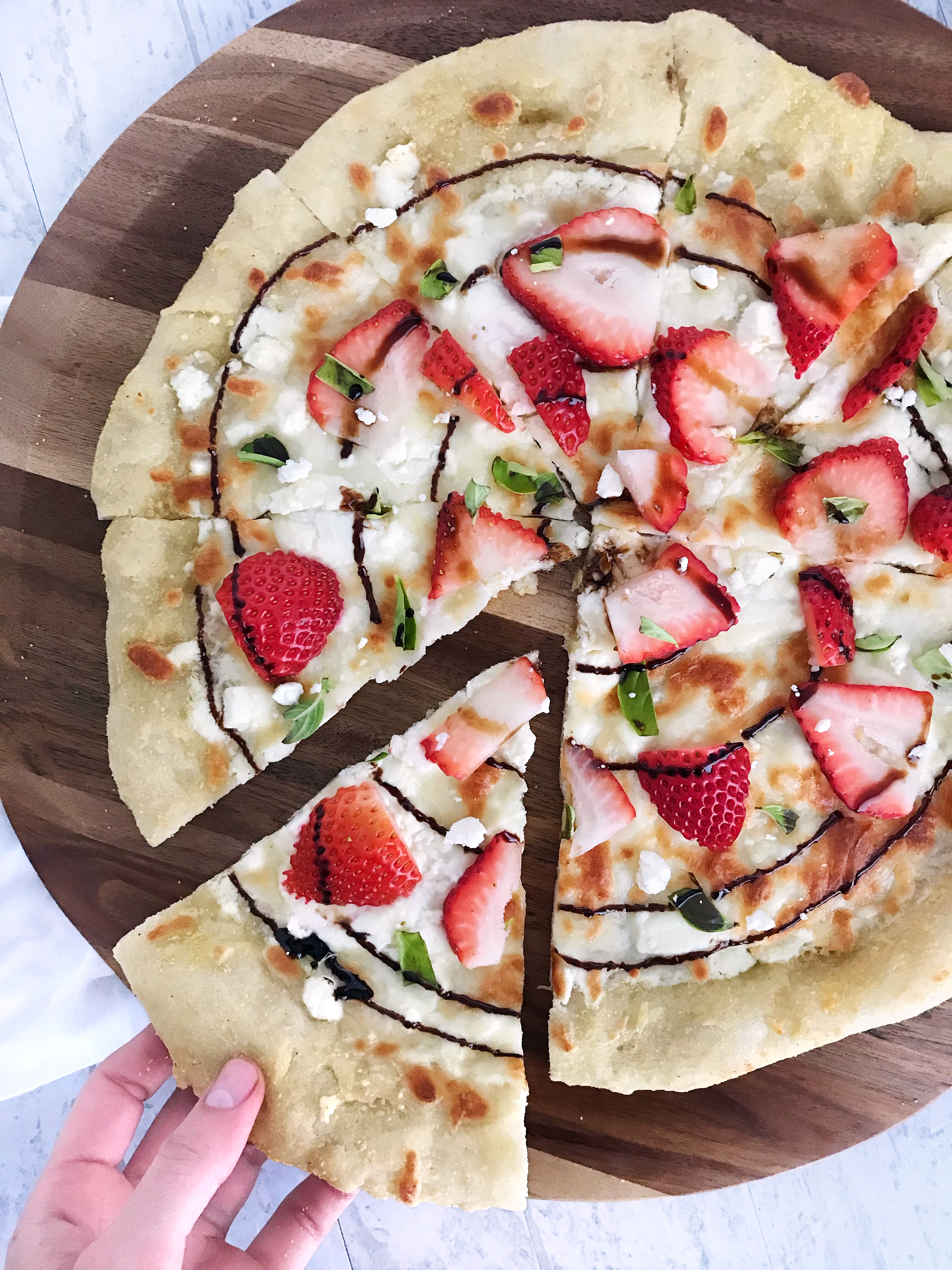 Strawberry balsamic pizza with hand grabbing a slice
