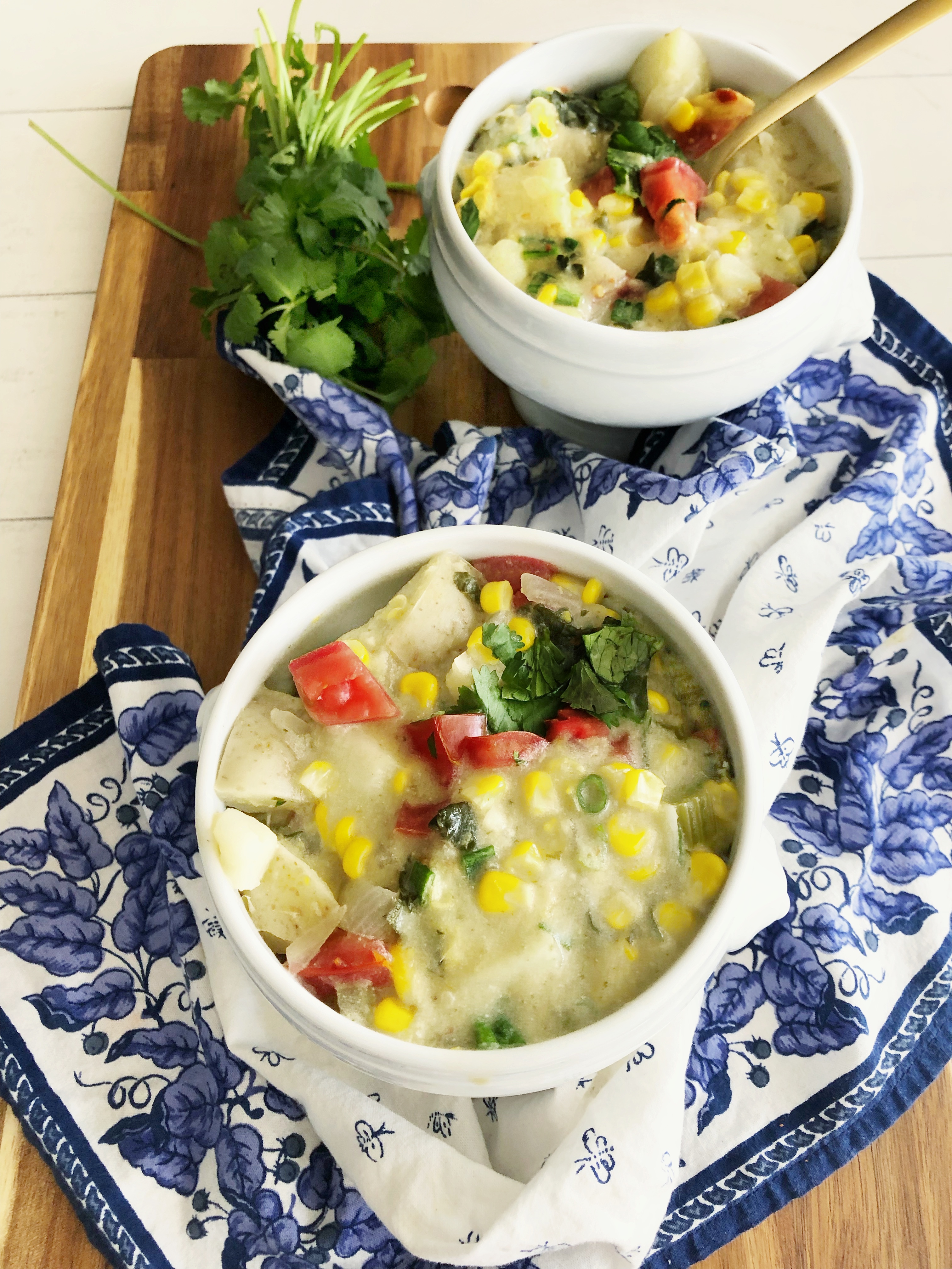 2 bowls of coconut corn chowder on a blue and white napkin and cutting board