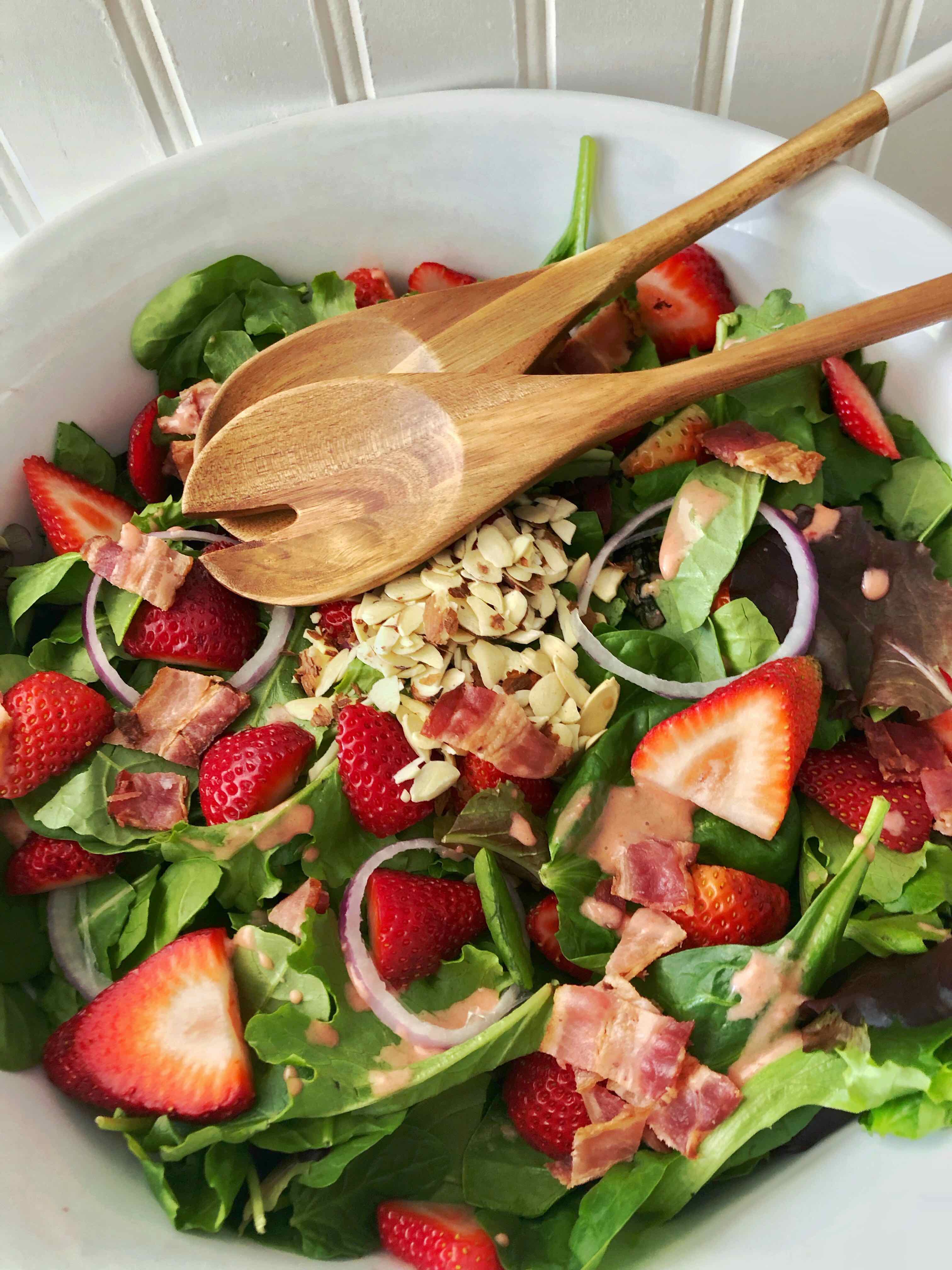 large white bowl with tongs filled with strawberry spinach salad