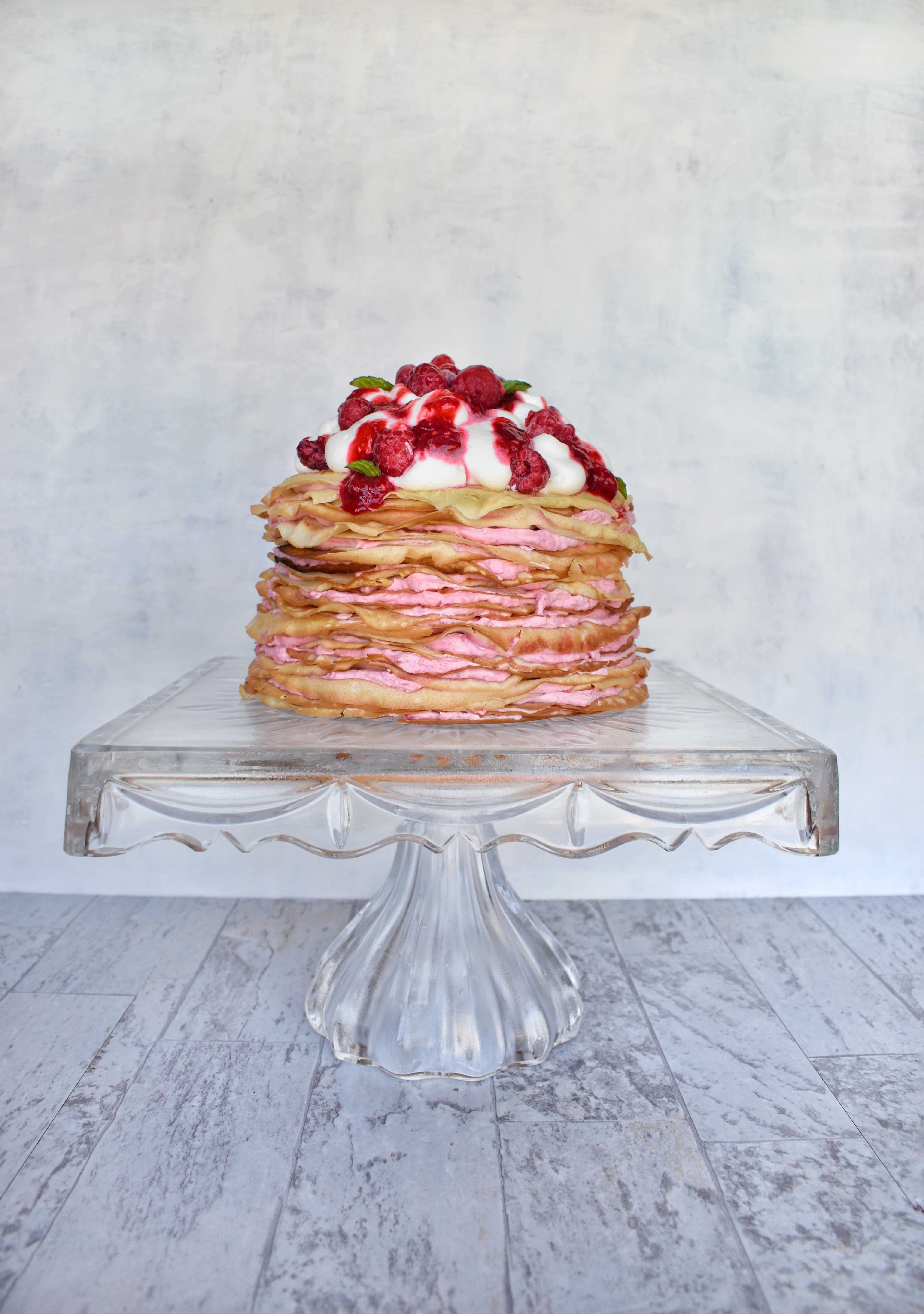 raspberry cream crepe cake on clear glass pedestal