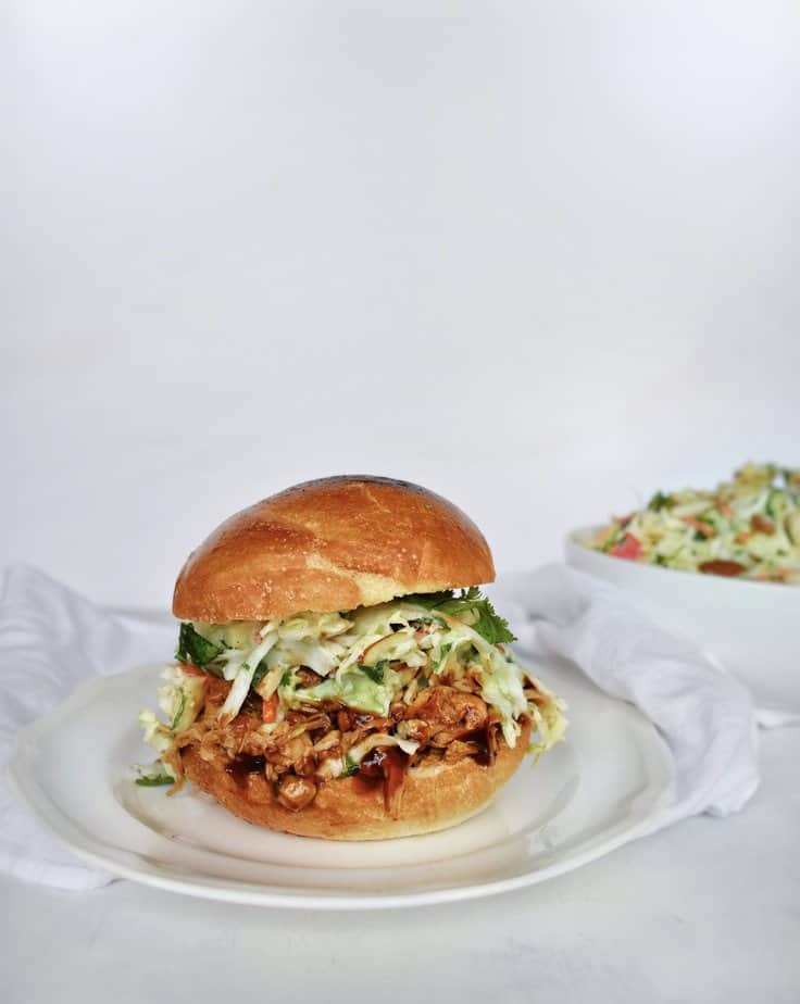 coleslaw on a pulled pork sandwich on a white plate