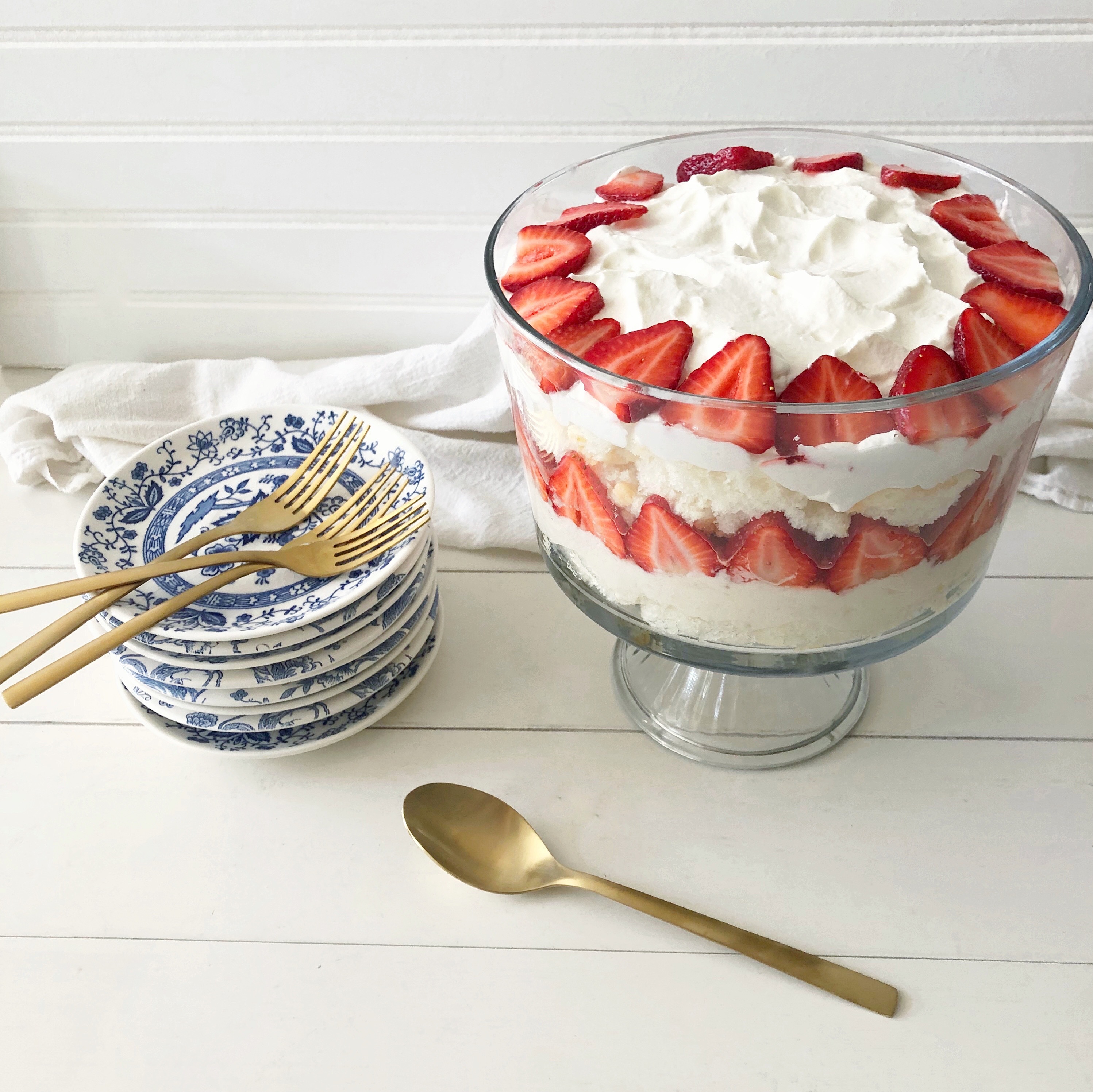 stack of blue & white plates with trifle bowl filled with strawberry lemon trifle