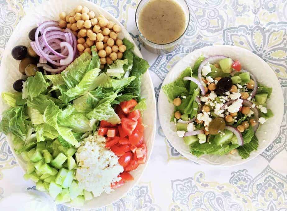 Greek salad on a platter with tossed salad on small plate and jar of vinaigrette