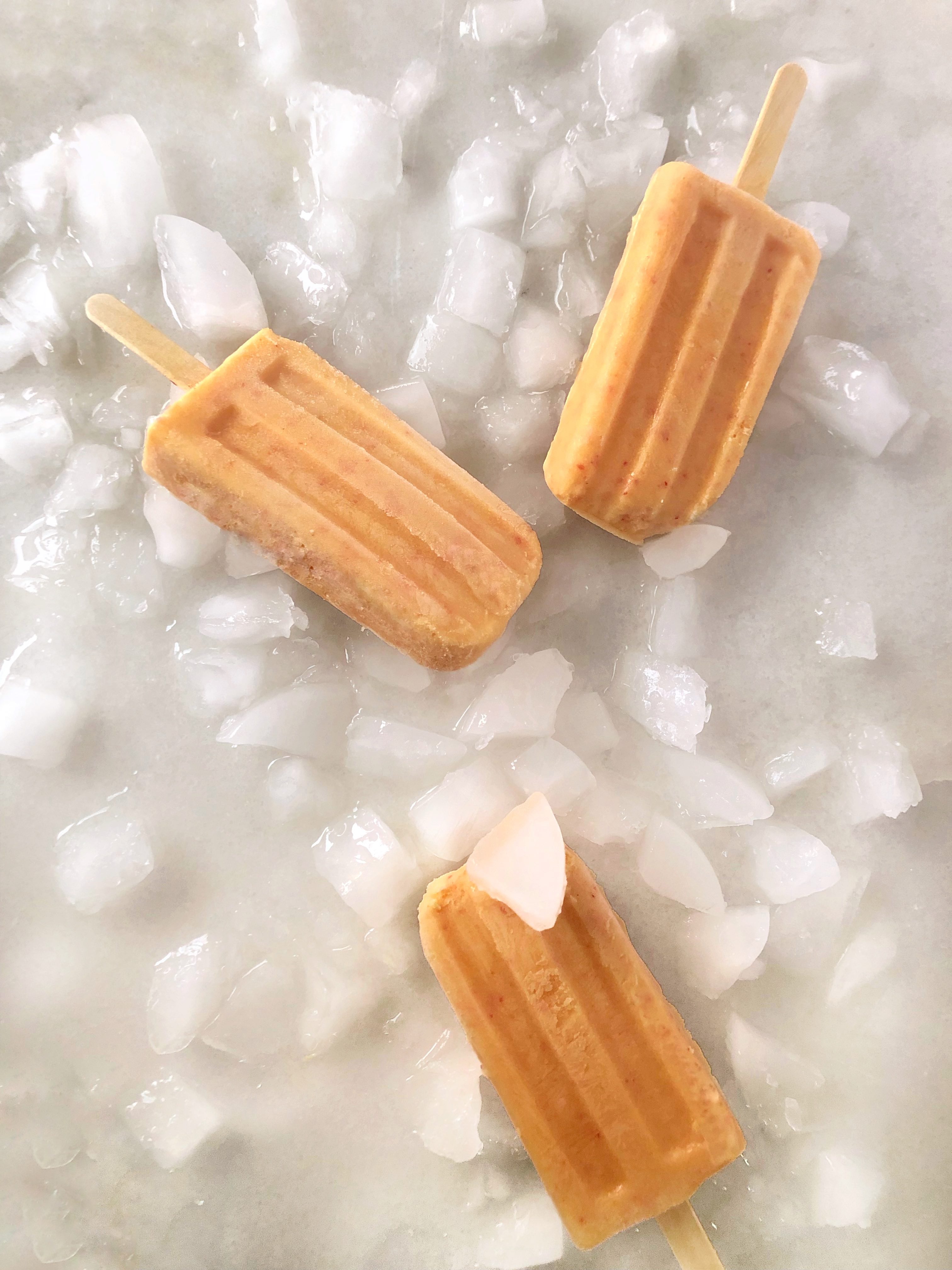 3 peaches and cream popsicles sitting on ice