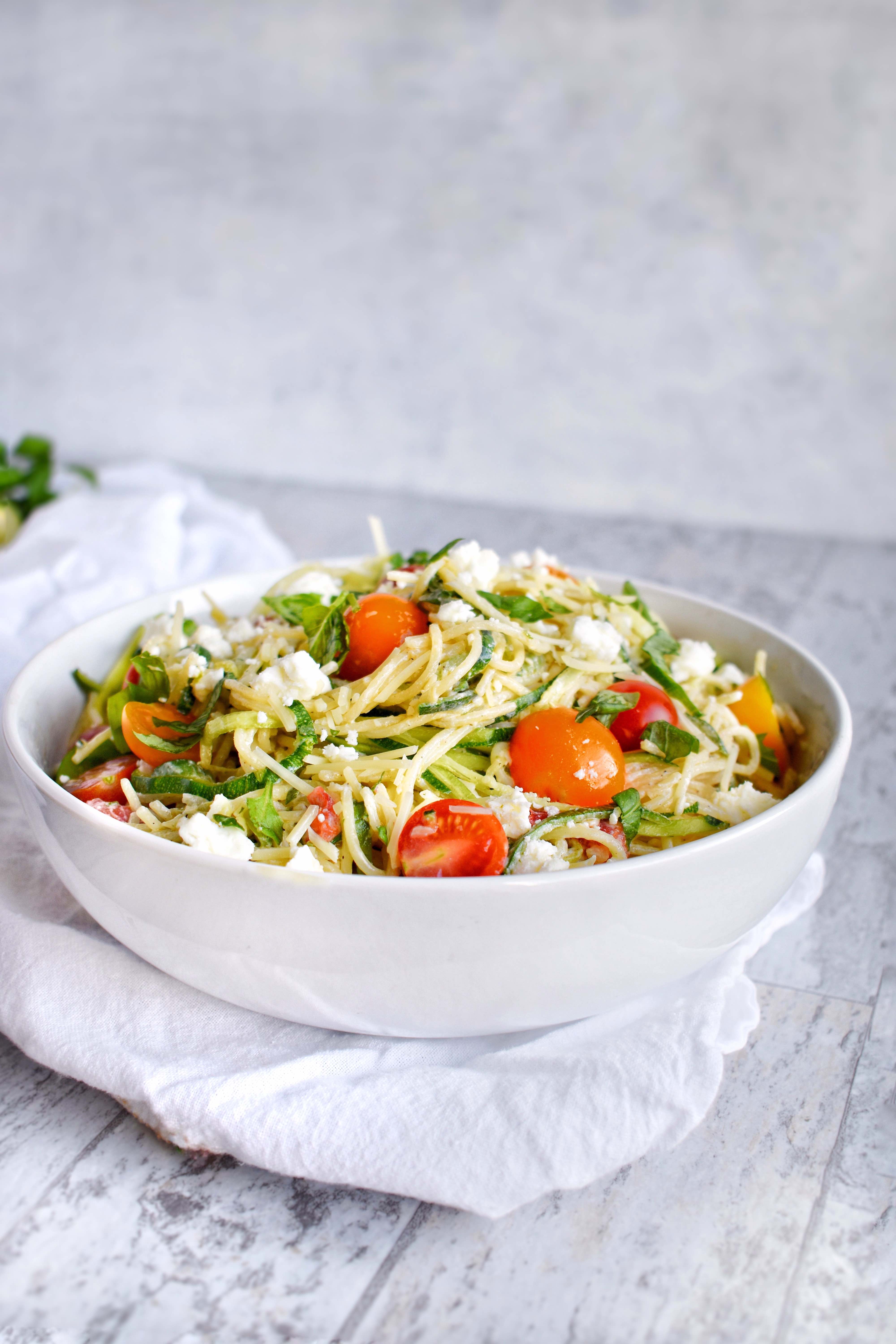 white bowl with zucchini noodle pasta toped with tomatoes and fresh herbs