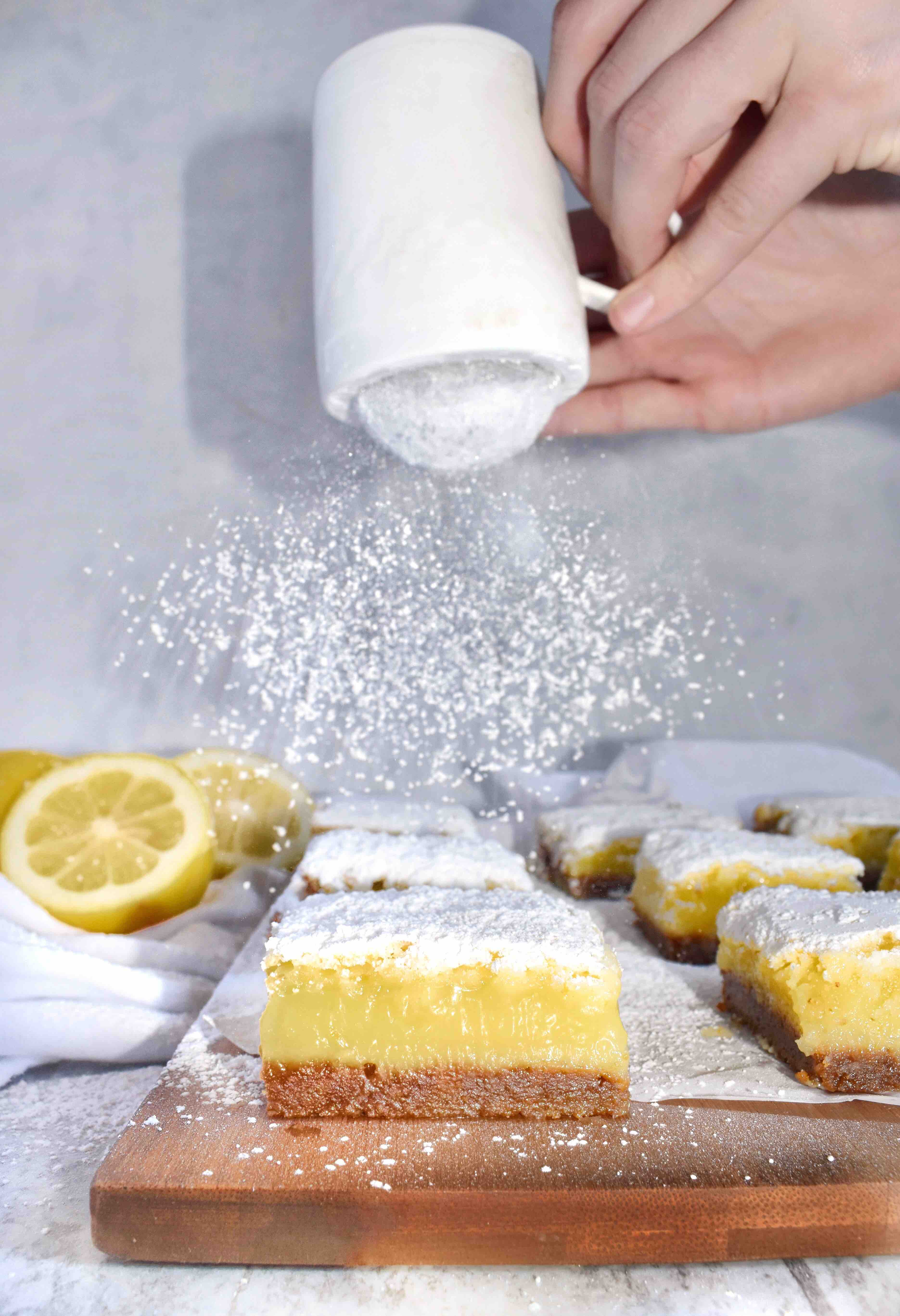 powder sugar being shaken over lemon bars with gingersnap crust