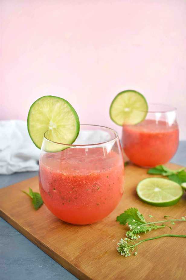 two glasses of watermelon drink sitting on a wooden board with pink background