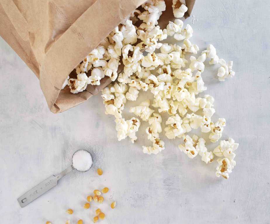 popcorn spilling out of paper bag with salt and popcorn kernels