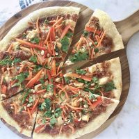 thai chicken pizza cut into slices on wooden board