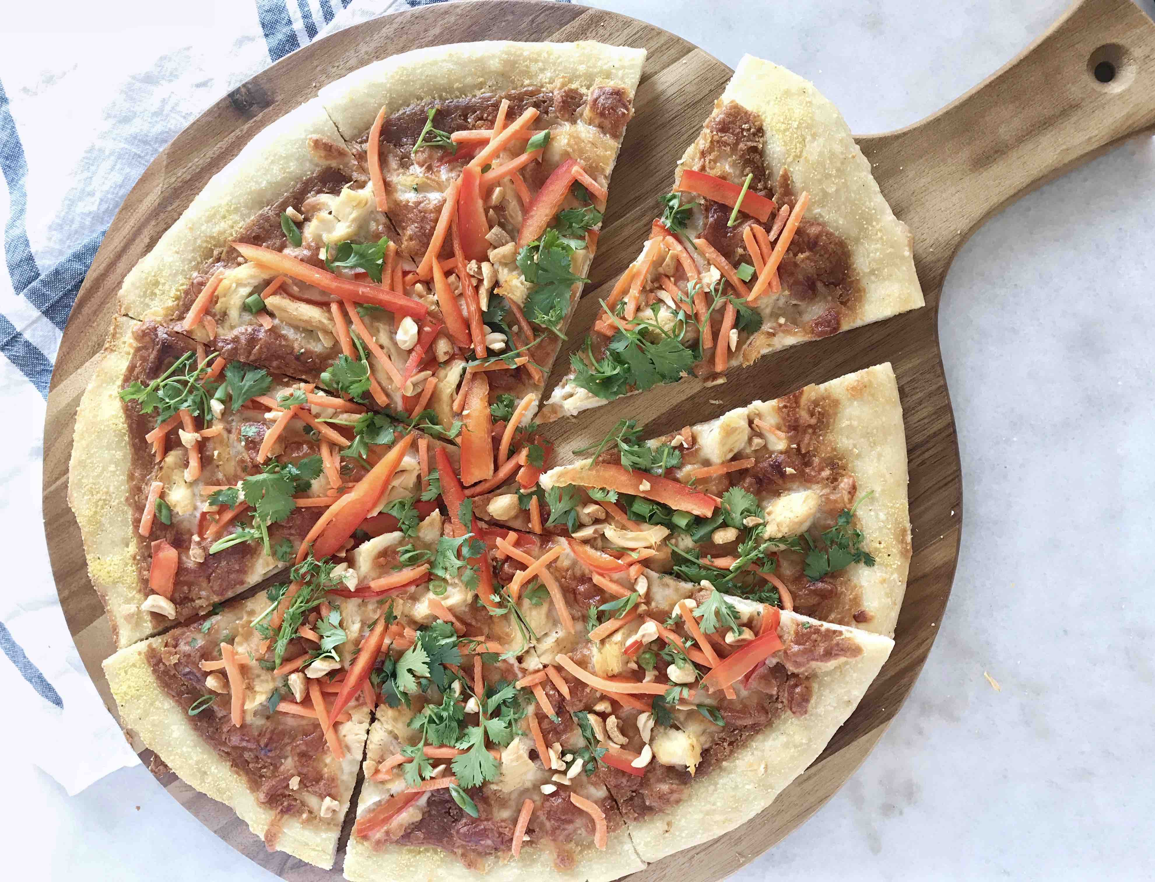 thai chicken pizza cut into slices on wooden board