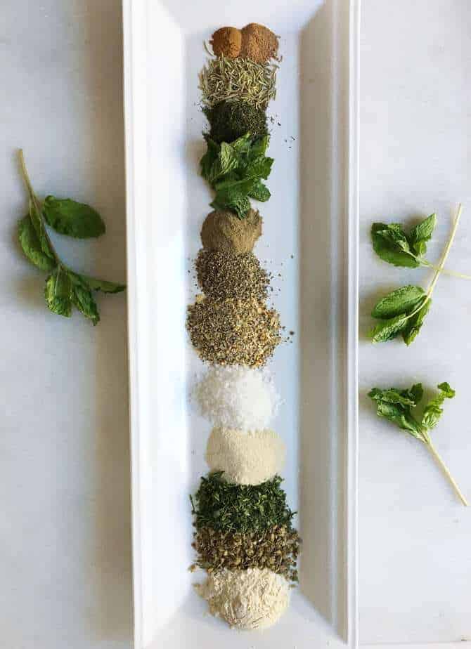 little piles of Greek herbs and seasoning lined up on white tray