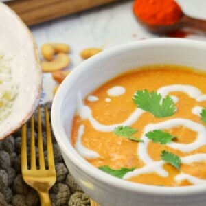 white bowl with red butter chicken and swirled cream.