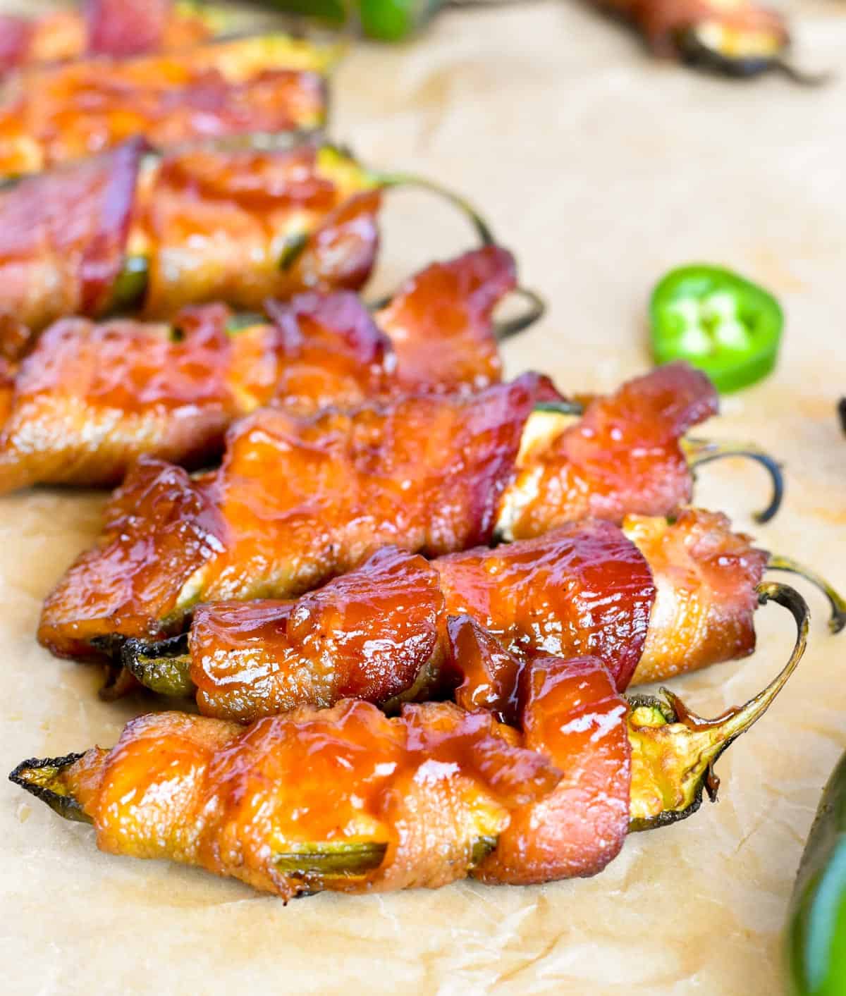 jalapeno poppers wrapped in bacon lined up next to each other on parchment paper.