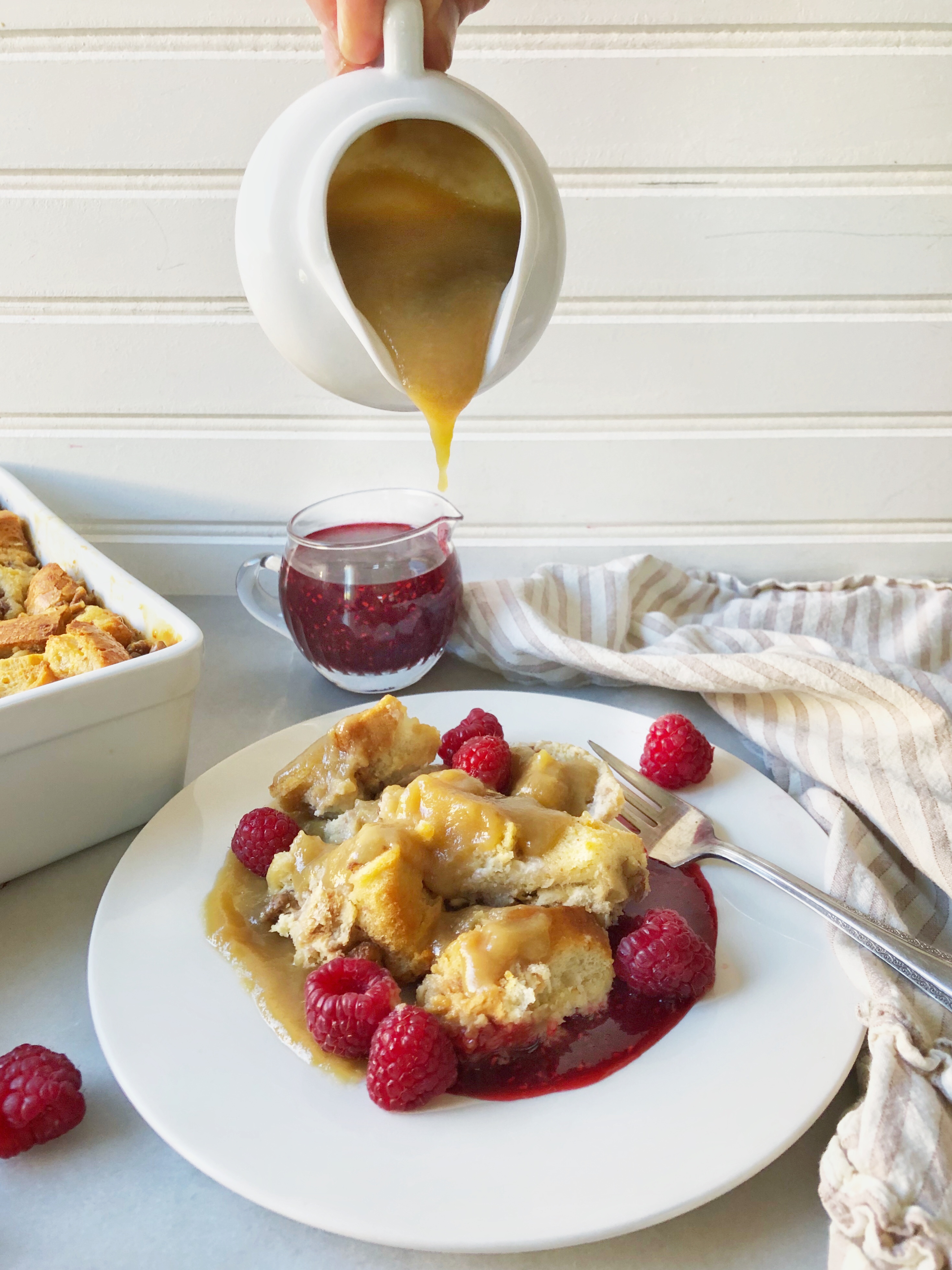 white chocolate bread pudding with raspberries and caramel sauce poured over it