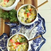 3 bowls of coconut corn chowder on a blue and white napkin and cutting board