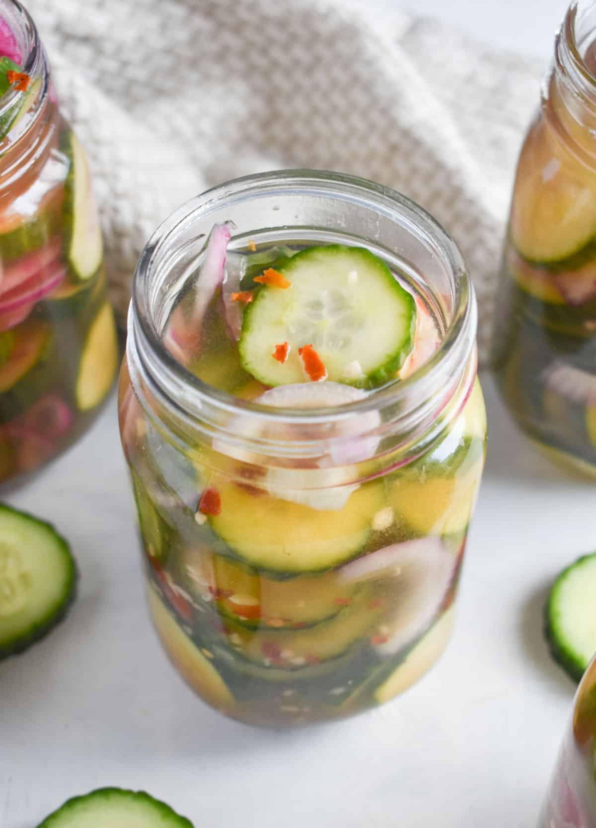 several jars full of pickles with lids off. 