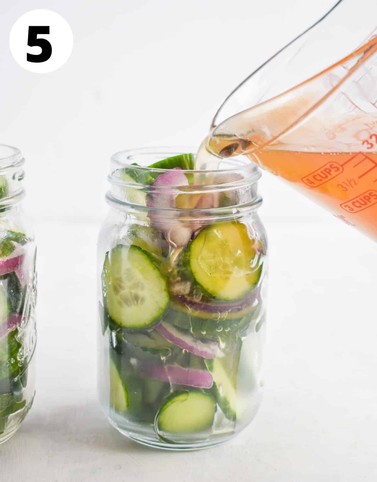 liquid being poured over cucumbers and onions in jar. 