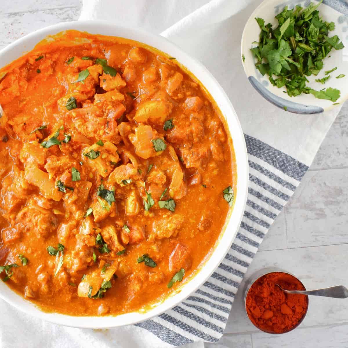 white bowl full of chicken tikka masala with spices on side.