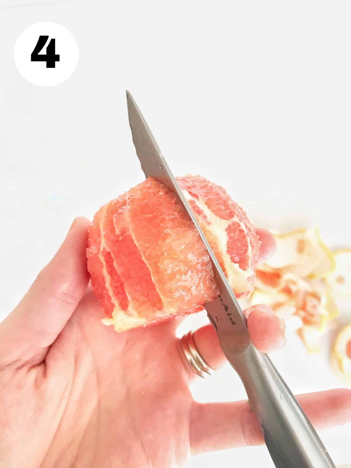 hand holding grapefruit with knife slicing between sections. 