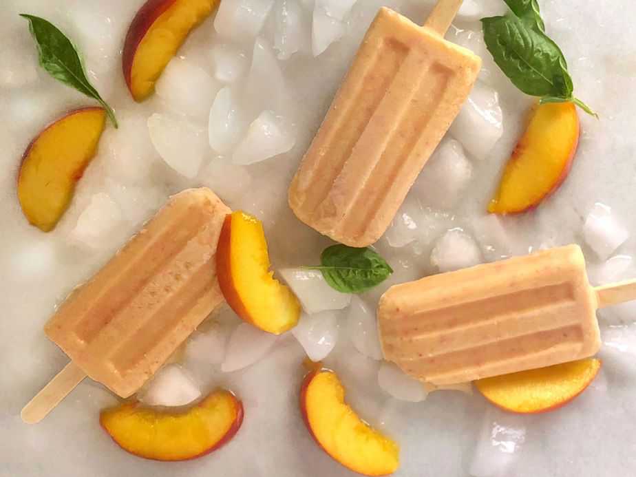 peaches and cream popsicles laying on ice with peach slices