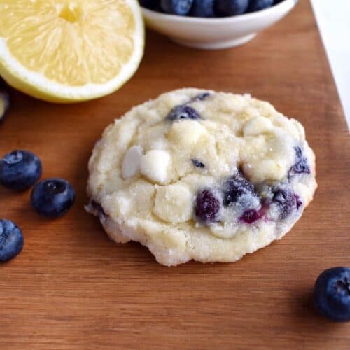 blueberry lemon cookie sitting on wooden board with fresh blueberries and half a lemon.