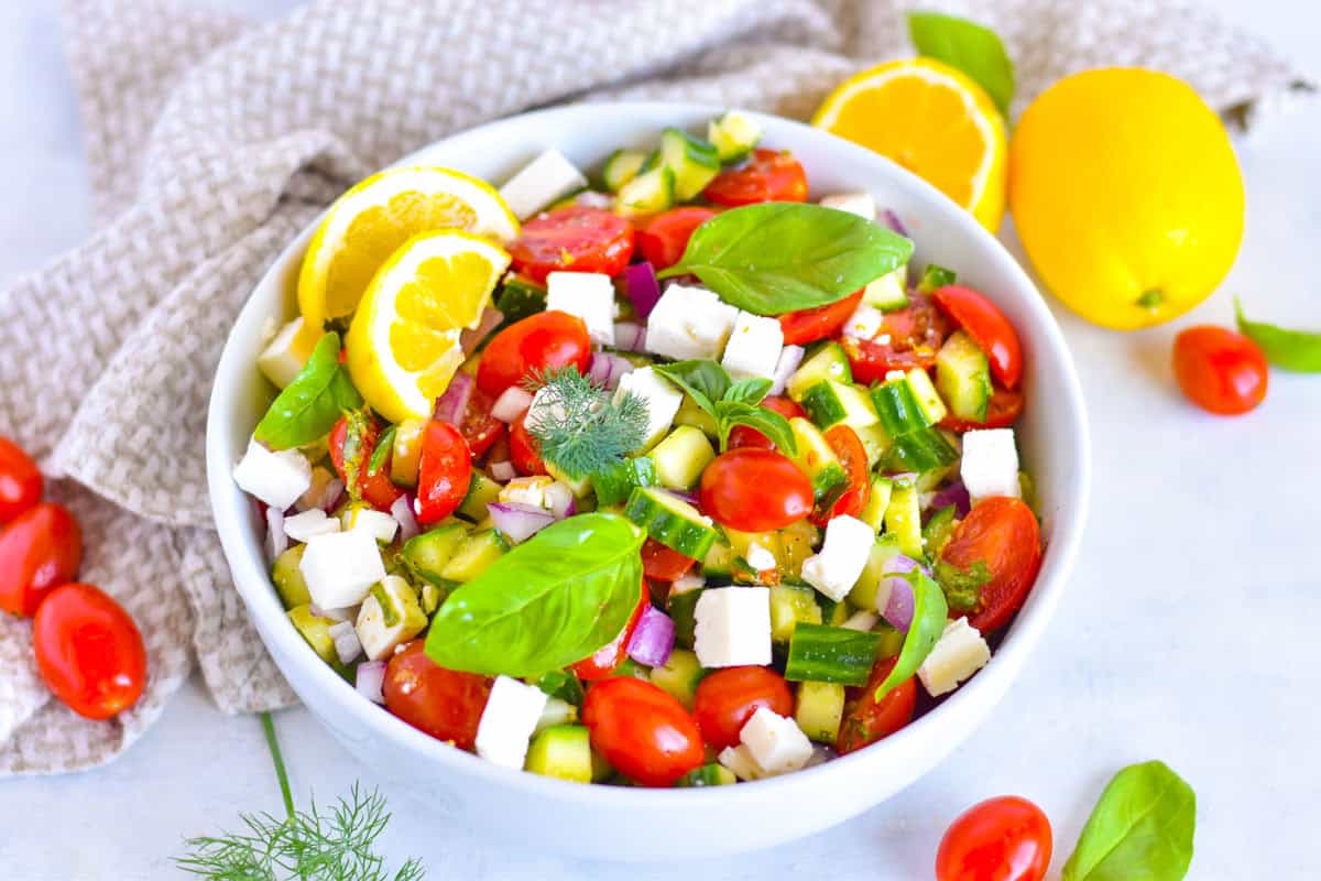 cucumber salad in white bowl topped with fresh herbs and lemon wedge.