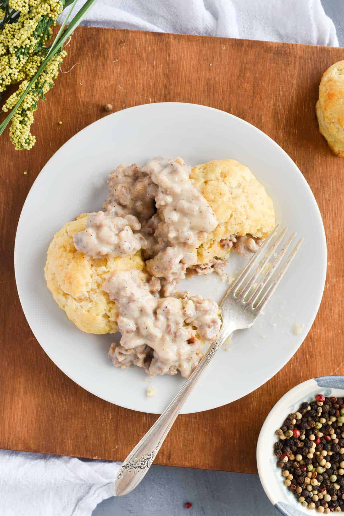 sausage gravy on biscuits on white plate with bite out of it. 