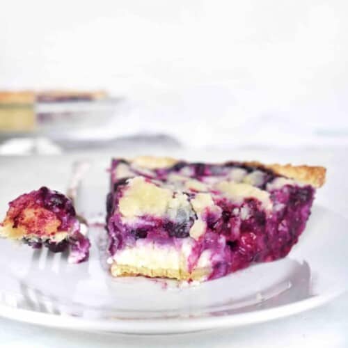 blueberry pie slice on plate with fork and bite out of it