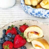 bowl of rolls and plate with cut open ham and cheese rolls and berries