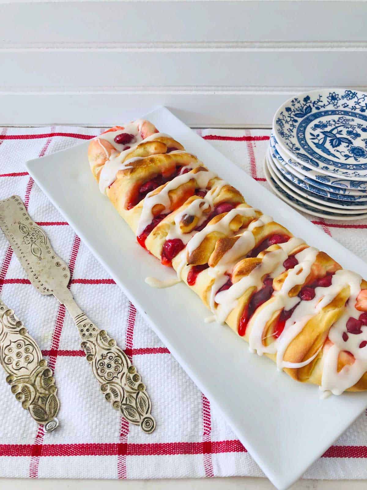 cherry cream cheese braid on white rectangle platter with silver serving pieces.