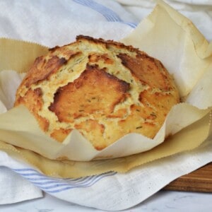 crisp loaf of herb and cheese bread laying on layers of parchment paper and linen cloths.