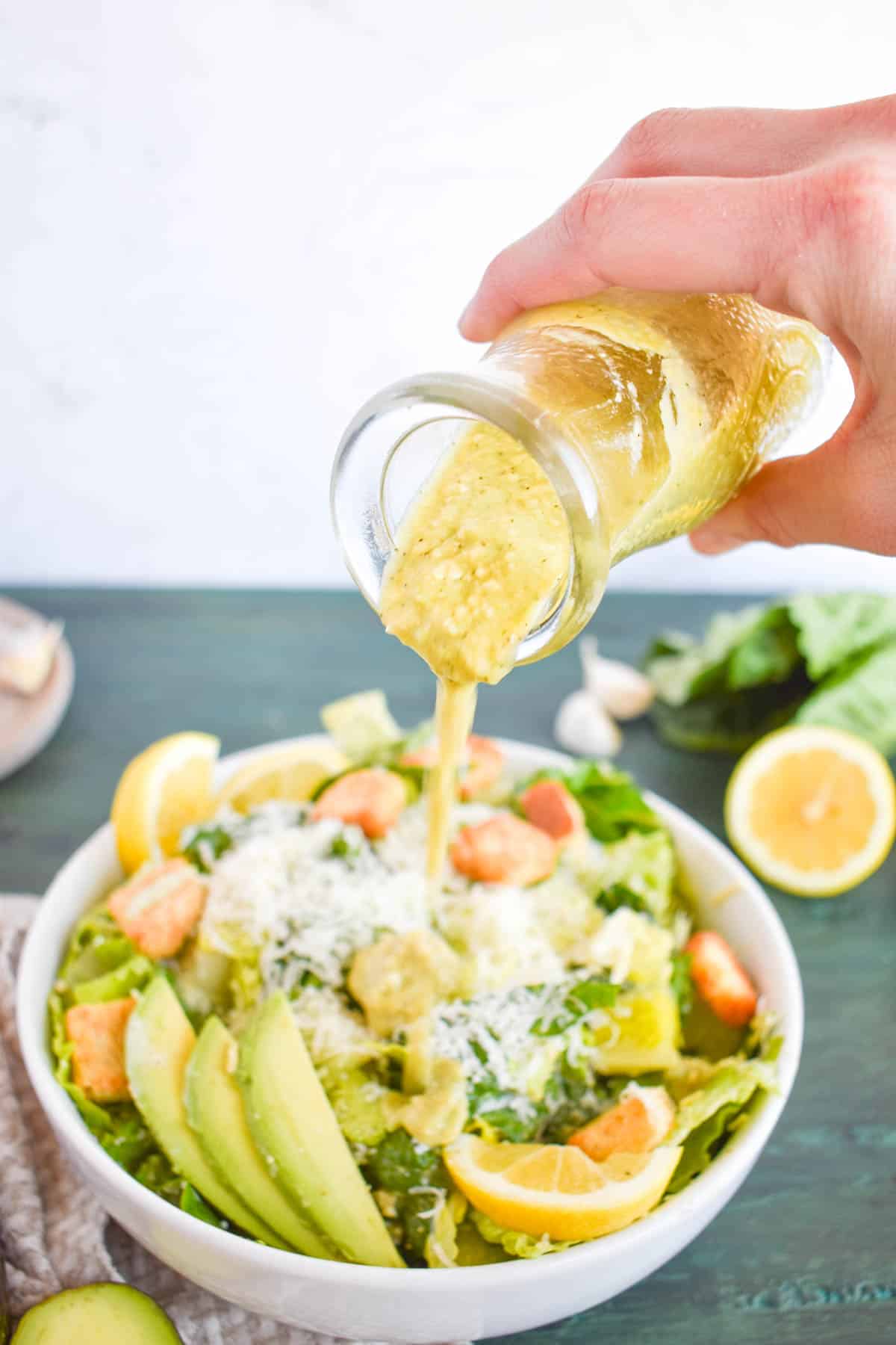 avocado caesar dressing being poured over salad in bowl. 