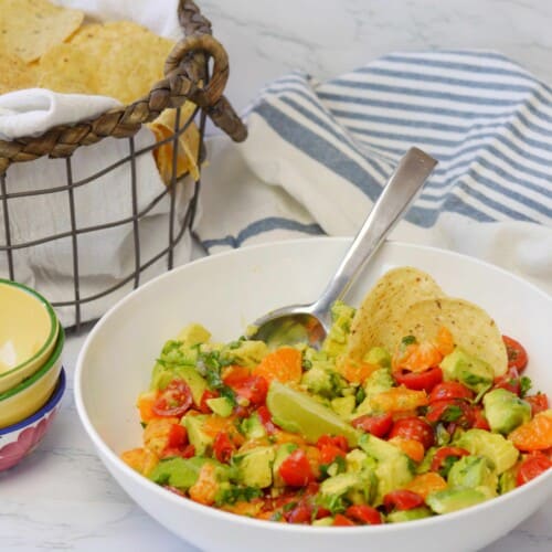 white bowl of mandarin guacamole with basket of tortilla chips