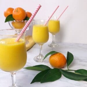 3 glasses filled with orange mango freeze and fresh oranges
