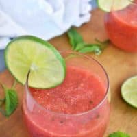 glass of watermelon slush sitting on a wooden board with a lime
