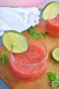 glass of watermelon slush sitting on a wooden board with a lime