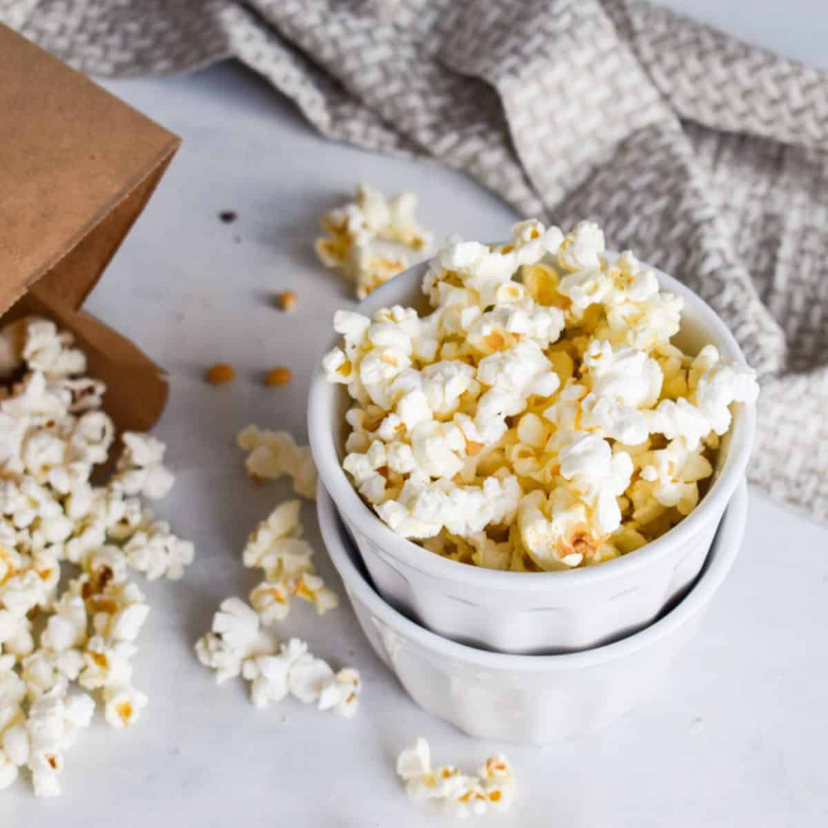 white cups filled with popcorn next to a brown paper bag with popcorn spilling out.