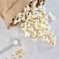 popcorn spilling out of paper bag with salt and popcorn kernels