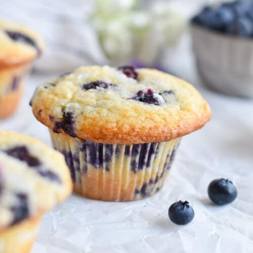 muffin on white parchment paper surrounded by fresh blueberries.